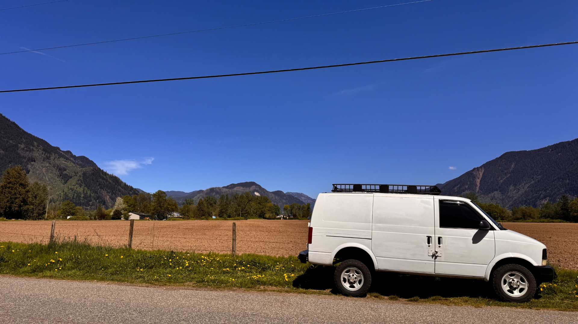 White van against tilled brown field, mountain ridges flanking the valley