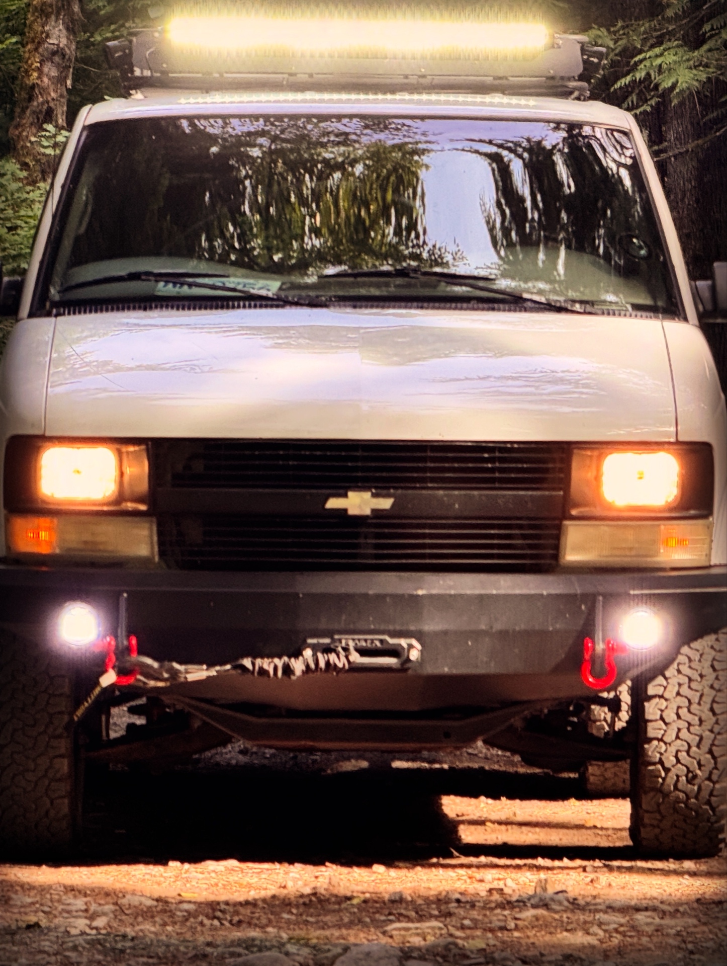 Dusk shot of the Astro with light bar and fog lights all on, parked deep in the forest