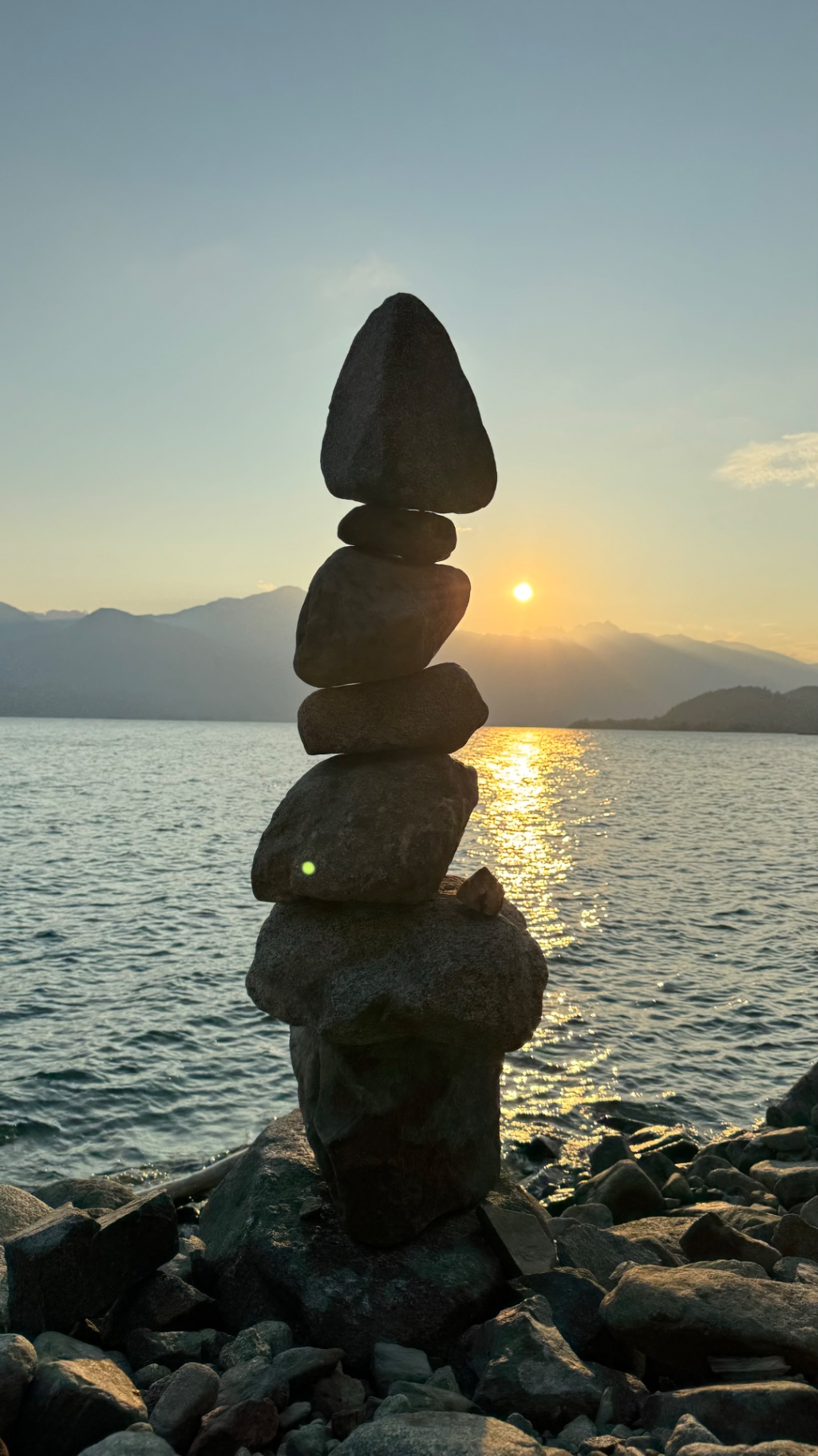 Stone cairn balanced on the lake's edge with the sun setting behind