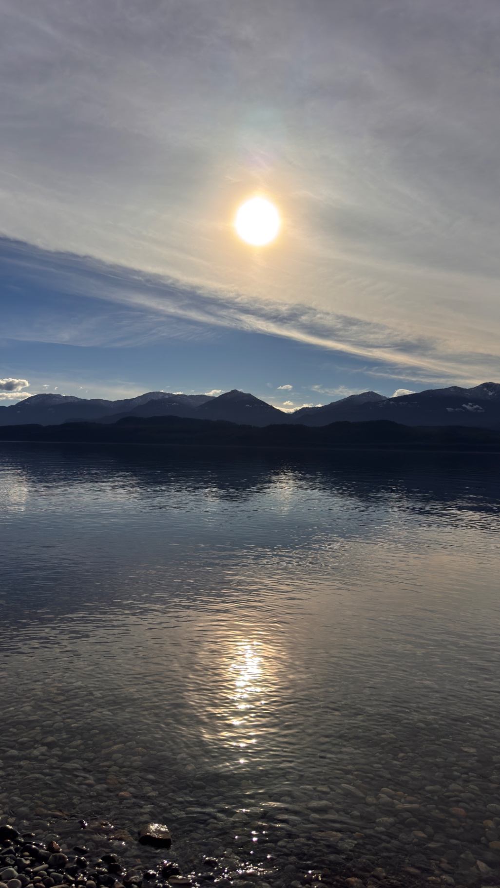Sun reflecting on calm lake water with mountains in background
