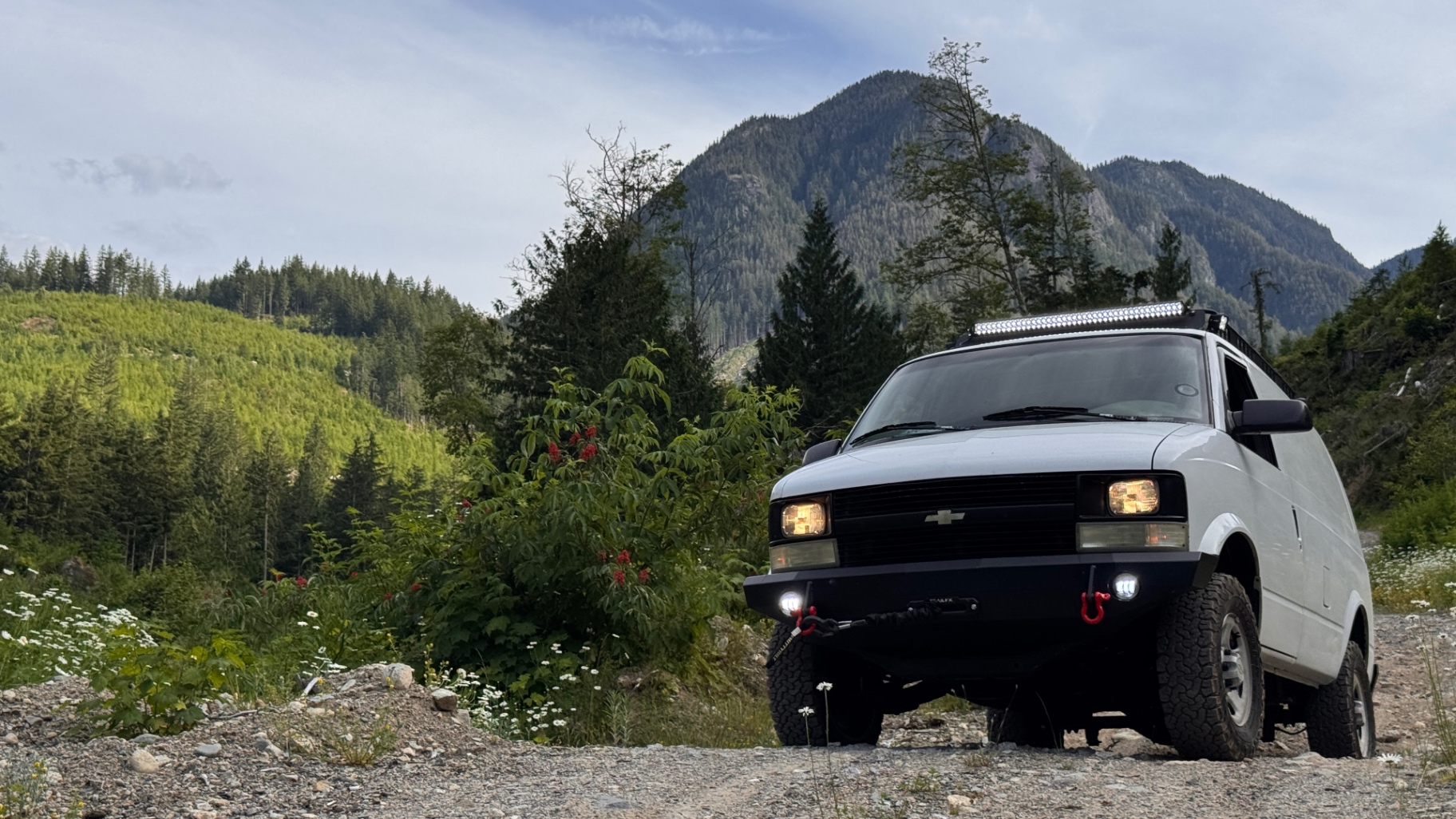 Astro parked on a gravel FSR pullout with a forested mountain rising in the background