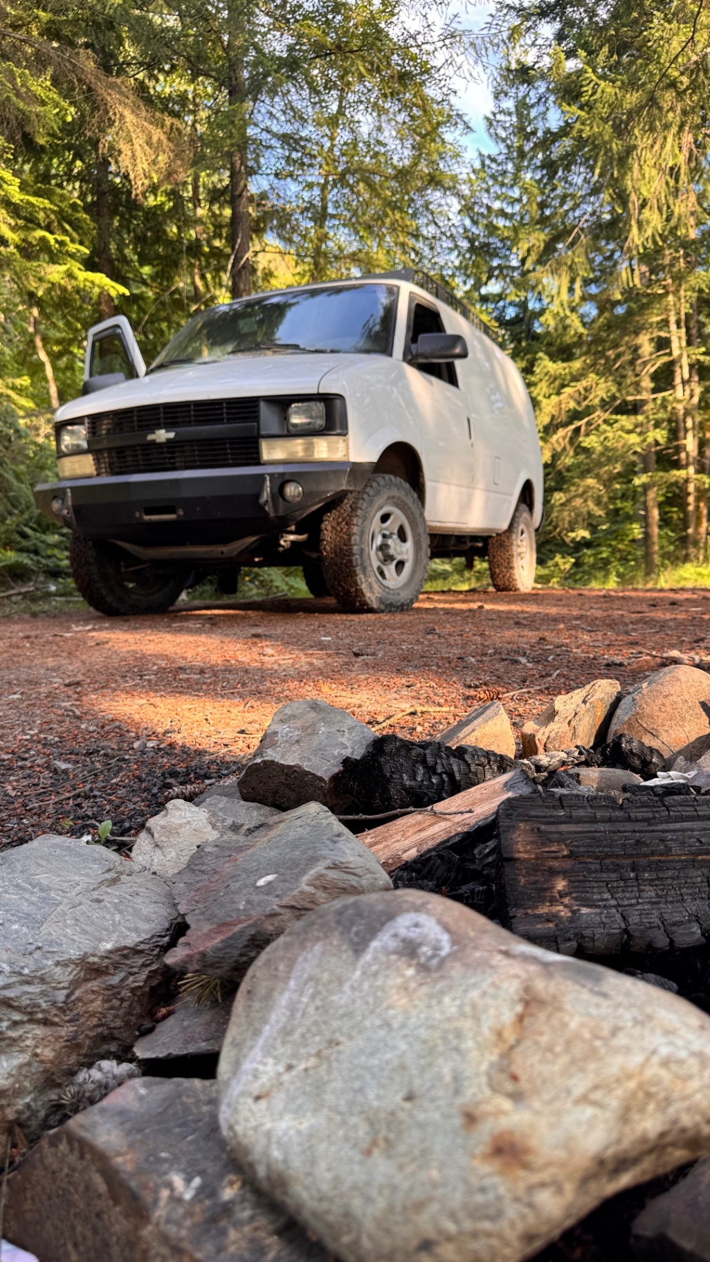 Van parked at a forest pullout with an old fire ring in the foreground