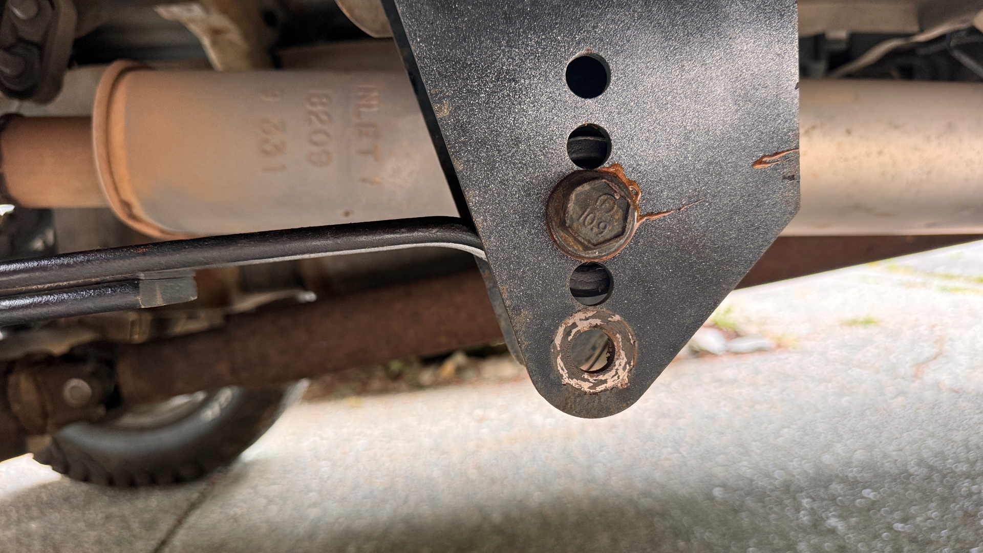 Close-up of the leaf spring hanger bracket showing the multiple hole positions used to reset the front-eye location and correct driveshaft angle.