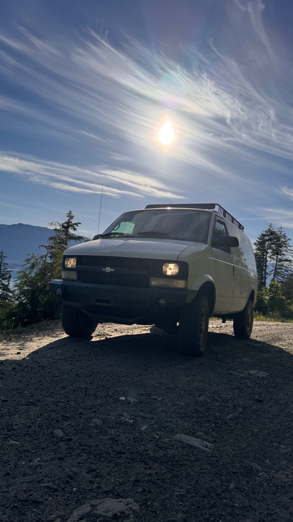 The Astro front-on with the sun flaring overhead at a lake-view pullout
